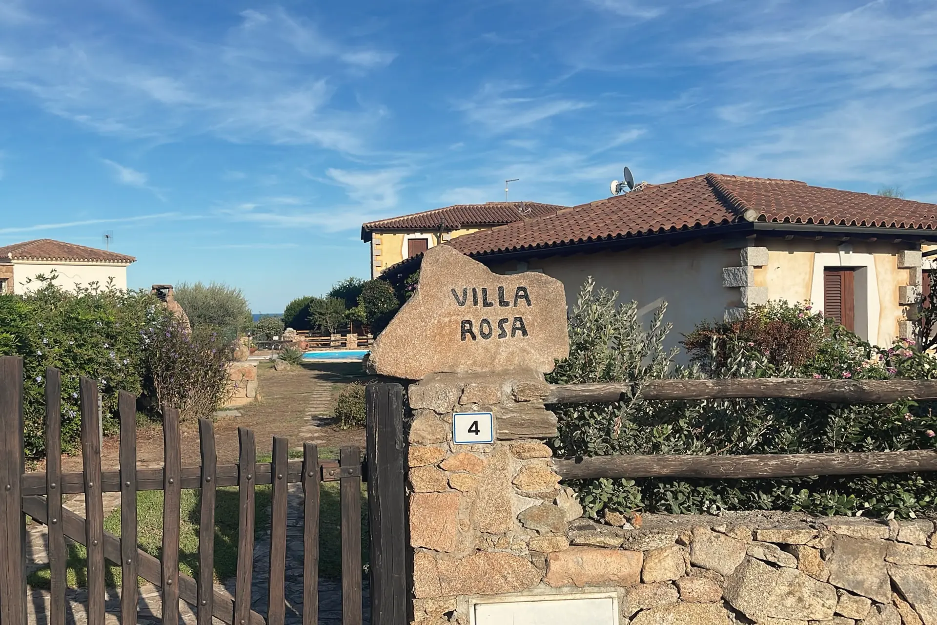 L’ingresso: il masso di granito con la scritta Villa Rosa, il cancello in legno e il numero 4, con la piscina in fondo al vialetto