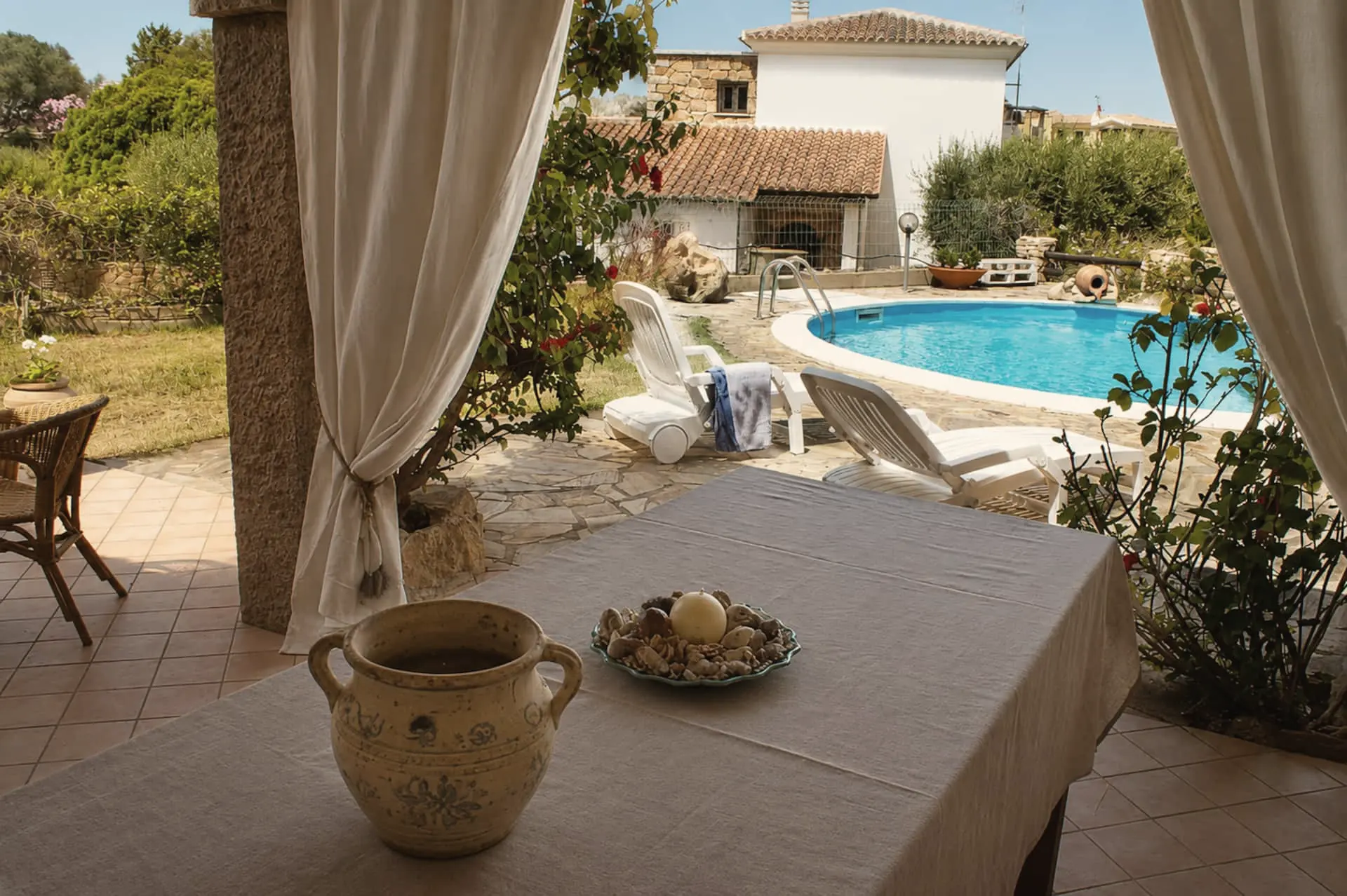 Il tavolo della veranda apparecchiato, con la piscina oltre le tende